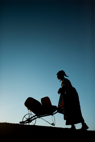 Silhouette of a woman pushing a pram on a hillside against a clear blue sky.