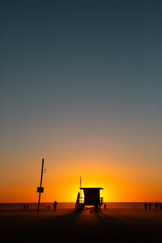 Silhouetted lifeguard tower and people on a beach at sunset.