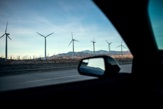 A scenic view from inside a car, showcasing wind turbines against a backdrop of mountains.