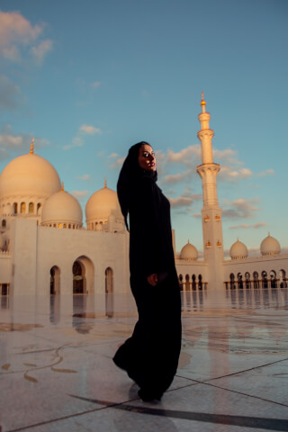 A woman in an abaya walking in front of the Sheikh Zayed Mosque in Abu Dhabi, UAE.