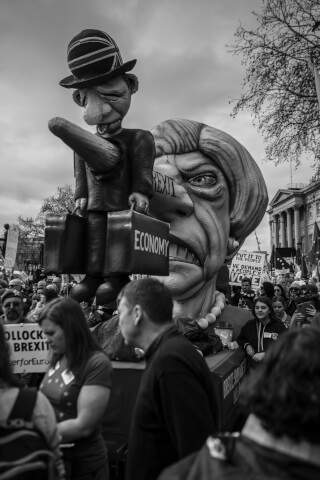 A black and white image shows a political protest with caricatures of political figures and signs.