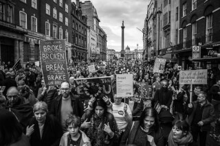 A black and white photo shows a large crowd of people marching in a city street holding signs.