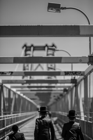 Three men in traditional clothing walk across a bridge in a black and white photograph.