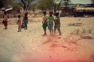 A group of children play together in a rural African village on a sunny day.
