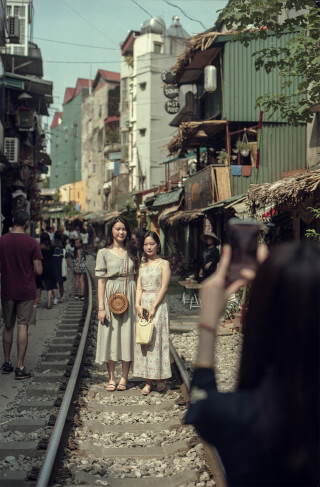 Two women pose on a train track amidst a bustling street in Hanoi, Vietnam, capturing the city's unique blend of charm and energy.