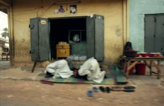Two muslim men praying outside a shop, respecting their religious tradition. Daily life.
