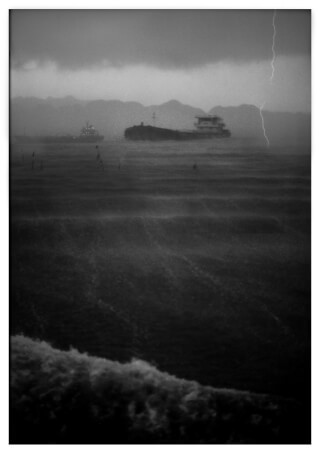 A dramatic black and white image features ships in a stormy sea, enhanced by a visible lightning strike.