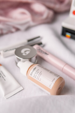 A collection of Glossier makeup and skincare products arranged on a white background.