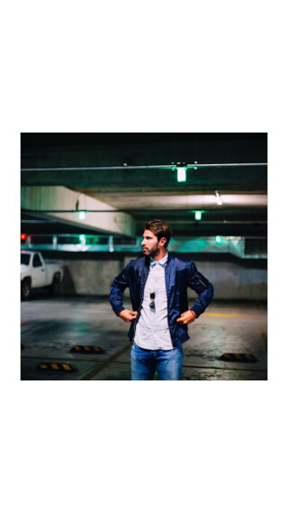 A stylish man in a parking garage, wearing a bomber jacket and jeans, looking confident.