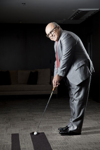 A businessman in a suit is putting golf indoors, embodying corporate wellness and a relaxed executive lifestyle.