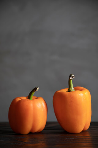 Two vibrant orange bell peppers sit on a wooden surface against a soft gray backdrop, perfect for food-related content.