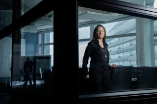 A businesswoman stands in a modern conference room with a city view, exuding confidence.