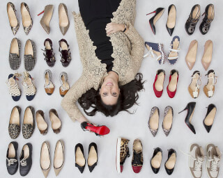 A woman lies surrounded by a variety of luxury shoes featuring the iconic red bottoms.
