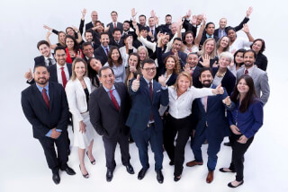 A large group of diverse business professionals smiling and celebrating success in a bright, corporate setting.