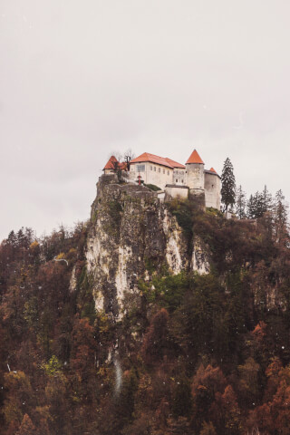 Bled Castle sits atop a cliff, overlooking autumn-colored trees in Bled, Slovenia.