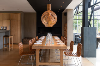 A modern dining room features a long wooden table set for a meal, illuminated by a unique lighting fixture.