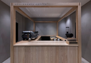 An inviting coffee shop interior features a modern coffee machine and grinder behind a light wood counter.