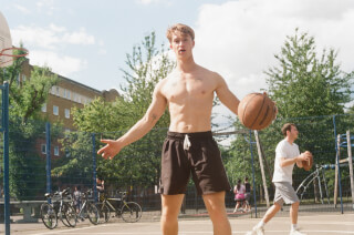 A fit man plays basketball on an outdoor court in summer, promoting a healthy and active lifestyle.