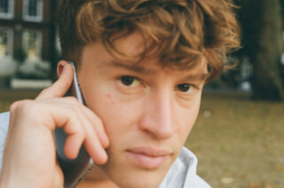 A young man is using a smartphone outdoors, engaging in a phone call with a calm expression.