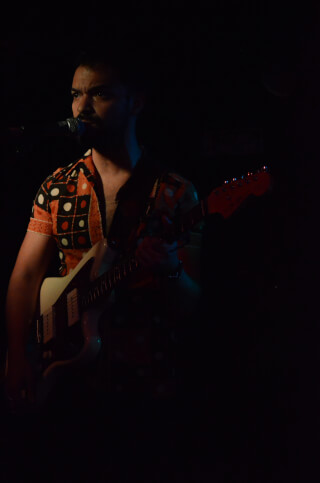A man passionately plays the guitar and sings on a dimly lit stage, bathed in warm, muted lighting.