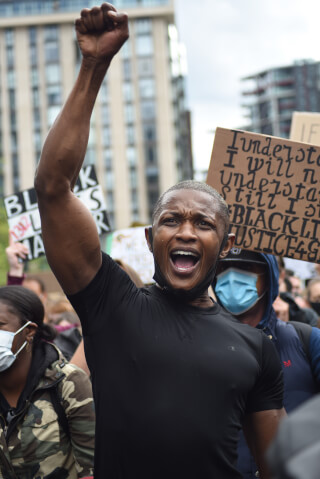 A man passionately protests with a raised fist during a demonstration on a city street.