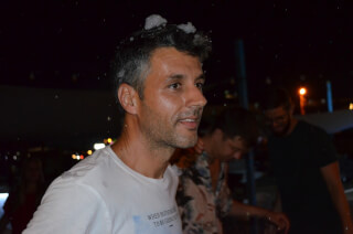 A man smiles in an outdoor night setting, enjoying a foam party with friends.