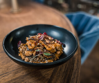 Close-up shot of chicken and lentils in a black bowl on a wooden table. 
