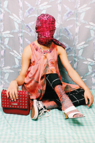A person in avant-garde fashion poses with a red purse, combining unique textures and styles for a bold statement.
