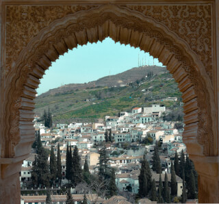 A scenic view of Granada, Spain, framed by an ornate arch, showcasing the city's architecture against a hilly backdrop.