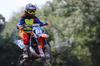 A young motocross rider soars through the air on their dirt bike in an action-packed outdoor scene.