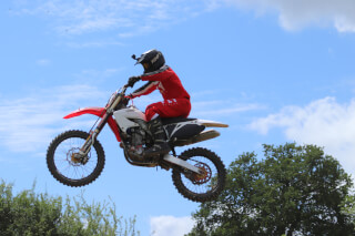 Motocross rider mid-air on a red dirt bike against a blue sky.