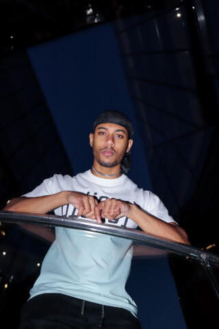 A confident young man poses at night with modern architecture in the background.