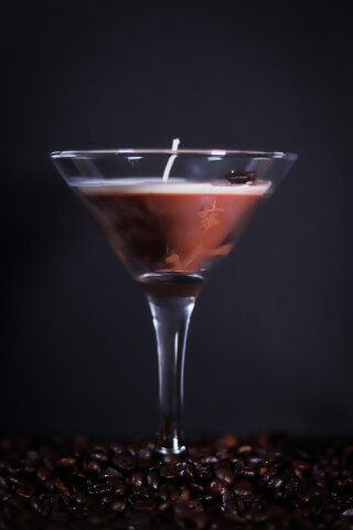 Coffee scented candle in a martini glass on a bed of roasted coffee beans for home decor.