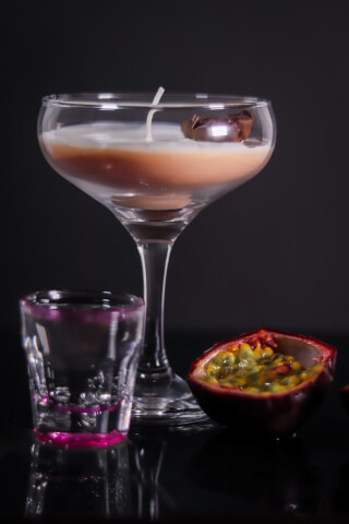 Still life of passion fruit and a candle in a cocktail glass on a reflective surface.