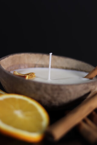 A coconut shell candle with orange slice and cinnamon for a relaxing home atmosphere.