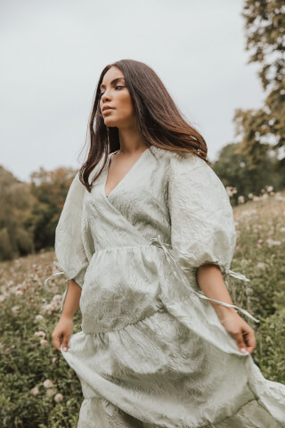 A brunette woman in a sage green dress walks through a field of wildflowers.