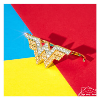 Close-up of a Wonder Woman logo ear cuff with gold and diamonds on a colorful background.