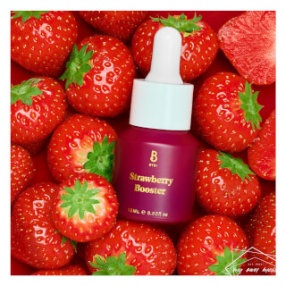 A bottle of BYBI Strawberry Booster skincare serum is surrounded by fresh strawberries.