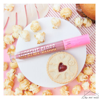 A pink lip gloss and heart cookie are displayed with popcorn for a beauty product promotion.