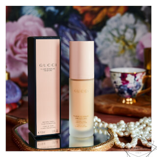 Elegant Gucci foundation in box and bottle on a reflective surface against floral backdrop, ideal for beauty promotion.