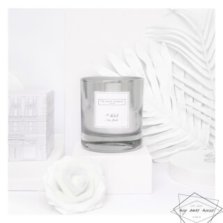 A silver candle by The White Company sits with a decorative box and white rose for a clean, elegant look.