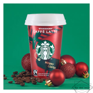 A festive Starbucks Caffe Latte is staged with coffee beans and Christmas ornaments against a green background.