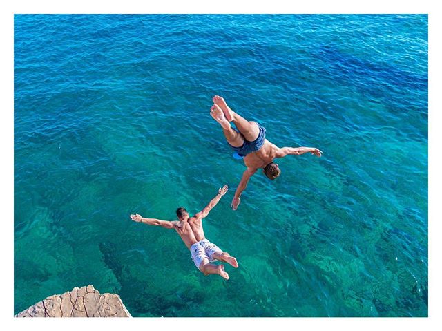 Two men cliff diving into the ocean. Active, summer lifestyle concept.