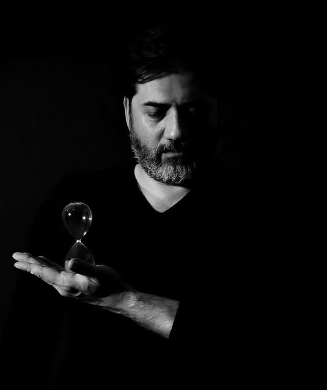 A man contemplates an hourglass in a dramatic black and white studio shot, symbolizing the passage of time.