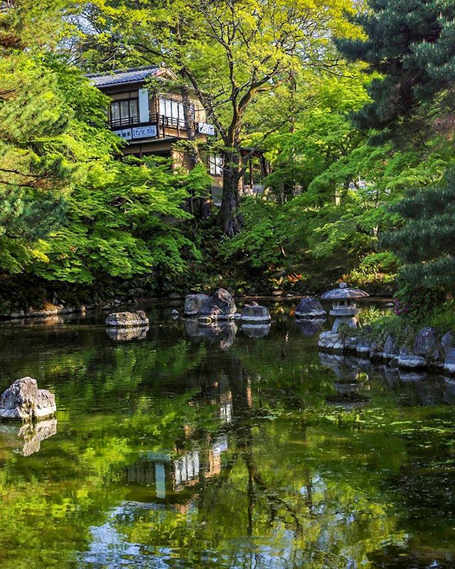 A tranquil Japanese garden with a pond reflecting trees and a traditional house.