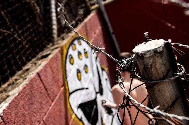 A man spray painting graffiti art on a wall behind barbed wire fence.