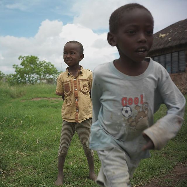 Two african children standing on a grassy field, captured in a candid and natural setting.