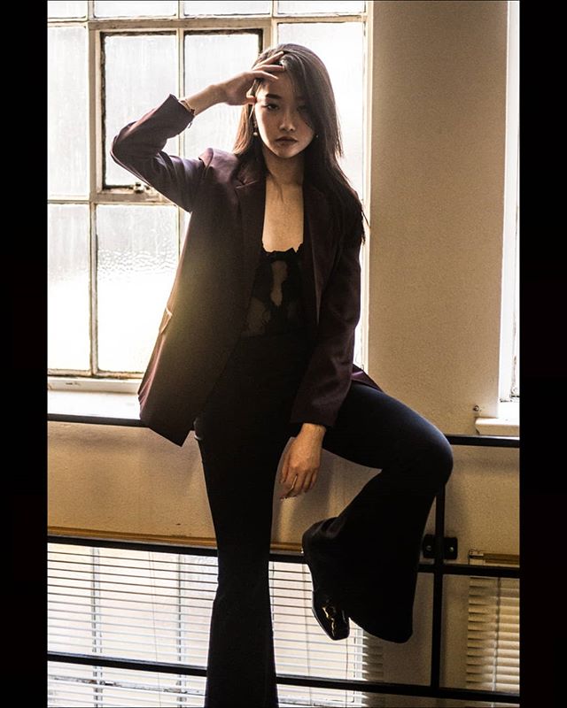 A stylish woman poses confidently in a blazer and flare pants by a window, exuding urban chic.