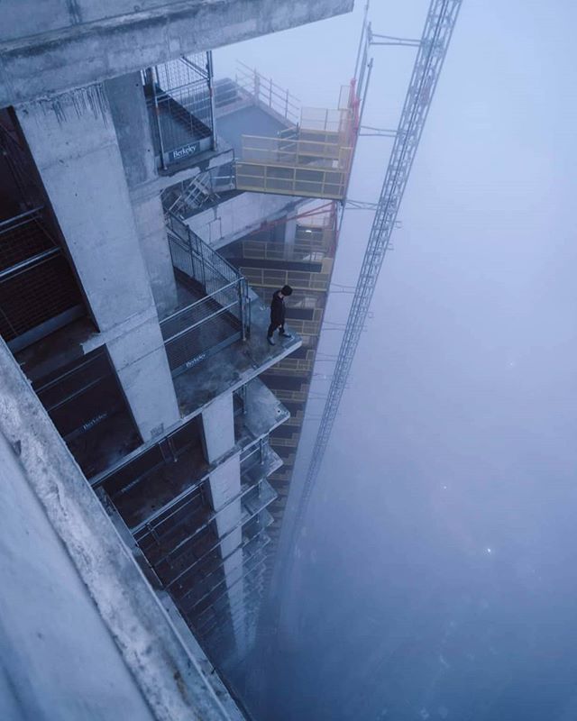 A man stands on the edge of an unfinished high-rise building shrouded in fog.