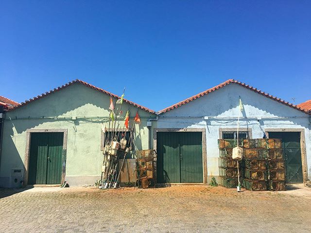 Picturesque view of colorful buildings with fishing gear and traps in a peaceful coastal village under a clear blue sky.